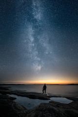 Wall Mural - Silhouette of a man standing alone by a sea and looking at sunset and the stars of the epic milky way