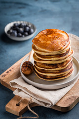 Stack of homemade pancakes with fresh blueberries and honey on blue background