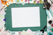 The cutting mat is surrounded by paper flowers, paper, tools and scrapbooking materials. Scrapbooking, top view, white blank sheet in the center