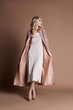 © angel_nt - Beautiful blonde woman posing in a pink coat on a beige background. Fashion show clothing, woman with perfect figure, long hair. Trendy fashionable autumn coat on the girl's body