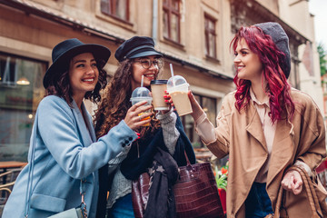 Three female friends having drinks outdoors. Women clinking coffee, orange juice and tea cups