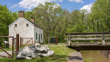 A White Stone Lock House Sits Alongside The C&O Canal And It's Adjoining Towpath, Which Meanders Through The Woods In Maryland. 