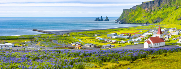 View of basalt stacks Reynisdrangar, black sand beach, church and city of Vik, Iceland