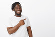 © Cookie Studio - Joyful friendly african-american bearded man in white t-shirt, pointing at upper left corner, smiling and laughing from happiness and positive emotions, being glad sharing amazing copy space