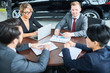 © Seventyfour - Group of business people discussing a contract together at car salon