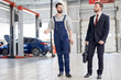 © Seventyfour - Full length portrait of modern bearded mechanic giving giving tour of workshop to handsome businessman walking across car service and repair center, copy space