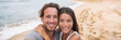 © Maridav - Tourists on beach Smiling beautiful young multiracial couple taking selfie on vacation panoramic banner crop. Asian woman, Caucasian man.