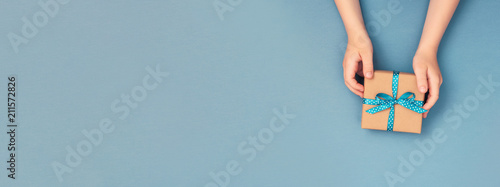 Child hands holding one gift box wrapped in kraft paper tied with blue ribbon...