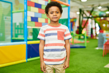 Wall Mural - colorful portrait of cute african-american boy standing and looking at camera in children play cente