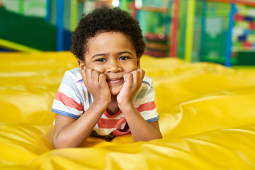 Wall Mural - colorful portrait of cute african-american boy smiling happily at camera while having fun in bouncy 