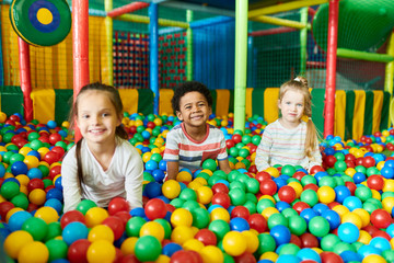 Wall Mural - colorful portrait of three happy little kids in ball pit smiling happily at camera while having fun 