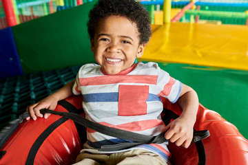 Wall Mural - colorful portrait of cheerful african-american boy sitting in tubing donut enjoying rides in childre