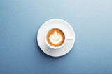 A cup of cappuccino with beautiful latte art on blue background. Top view, central composition.