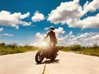 Biker girl stand up on modern classic motorcycle with blue sky and fluffy clouds. Freedom and outdoor lifestyle sport women concept. 