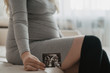 © GolubaPhoto - Young pregnant woman sitting at home and holding her recent ultrasound picture