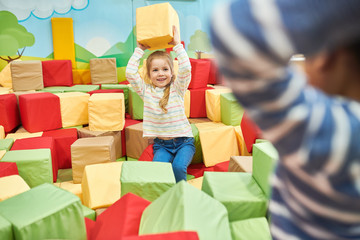 Wall Mural - colorful portrait of happy little girl playing in foam pit of trampoline center throwing foam cubes 