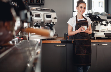 Young smiling cafe business owner standing at bar in coffee shop