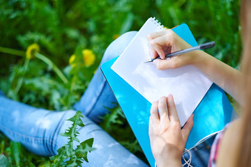 teenage girl student writing in notebook in park. Preparation for exams at college or university