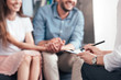 © LIGHTFIELD STUDIOS - cropped image of female counselor writing in clipboard while couple sitting on sofa and holding hands of each other in office