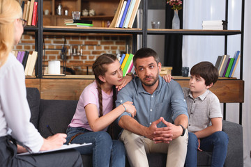 children cheering up father while he talking to female counselor on therapy session