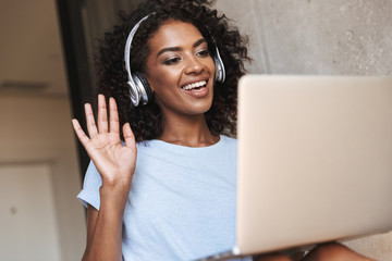 Wall Mural - Smiling african woman in headphones using laptop computer