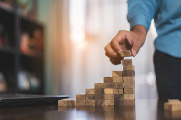 Businessman planing and strategy putting wooden blocks risk or success project stack of danger tower hands playing challenge game building construction protect at office.