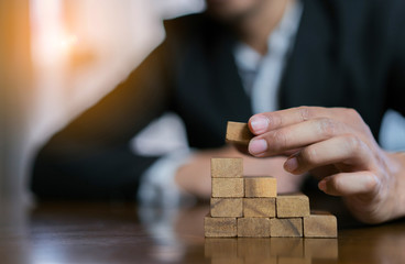 Businessman planing and strategy putting wooden blocks risk or success project hands control stack of danger tower challenge game building construction protect at office.