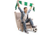 Overjoyed teenage soccer fan with a scarf and a football sitting in an armchair