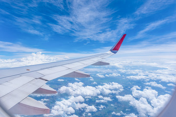 Wing of an airplane flying above the clouds look from cabin window.