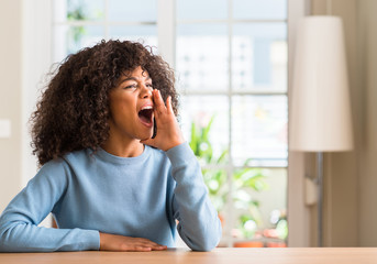 Poster - African american woman at home shouting and screaming loud to side with hand on mouth. Communication concept.