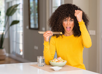 Poster - African american woman eating asian rice at home annoyed and frustrated shouting with anger, crazy and yelling with raised hand, anger concept