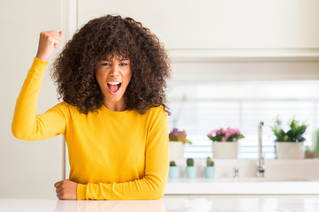 Poster - African american woman wearing yellow sweater at kitchen angry and mad raising fist frustrated and furious while shouting with anger. Rage and aggressive concept.