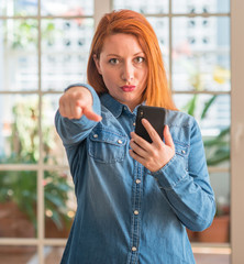 Sticker - Redhead woman using smartphone at home pointing with finger to the camera and to you, hand sign, positive and confident gesture from the front