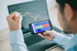 © chompoo - Hand of trader holding mobile phone touch screen showing buy and sell in Stock market order and blurred bakcground of laptop show financial chart, business trading concept