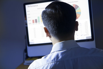 Wall Mural - Rear view of an Asian businessman reviewing financial reports and statistic in the office.