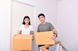 © S photographer - Moving house Concept. Asian young man is carrying his belongings. Young Asian women are holding their stuff in a paper box. Young are happy in the new house.