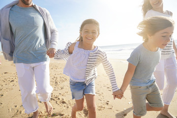 Wall Mural - Family running on sandy beach at sunset