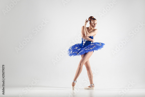 Fotografie, Obraz Young beautiful ballerina with bun collected hair wearing blue dress and pointe