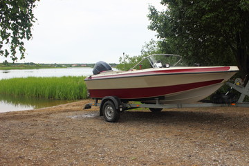 Wall Mural - Outdoor activities - descent of a white-red motor plastic boat on a trailer with a car on the water on a sandy slipway on the background of the river and the shore with green trees