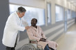 © JPC-PROD - African ,American,male doctor greeting recovering senior patient in wheelchair in hospital, hands on shoulder