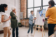 © Seventyfour - Full length portrait of female artist presenting modern watercolor painting to audience standing in art-studio or gallery
