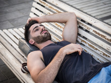 Attractive Young Man Resting On Wood Bench Outdoor In City Park During The Evening