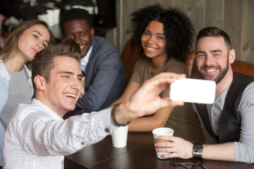 Diverse colleagues taking group photo on smartphone spending time together in coffeeshop, smiling multiracial millennial friends making self-portrait, sitting at coffee table having fun in cozy cafe