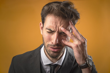 Young business man having a strong headache and pain, orange background, studio image