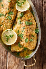 Canvas Print - Baked trout fish with garlic lemon butter sauce, parsley closeup in a copper pan on a table. Vertical top view