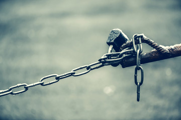 Closed padlock on chain of brown fence is close-up on background of asphalt with bokeh with copy space. Backdrop with lock of parking place. Image of checkpoint in blue faded tones.