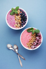 Wall Mural - Two smoothie bowls with granola, blueberries, raspberries and mint on blue background. Healthy breakfast, top view.