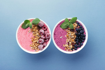 Two smoothie bowls with granola, blueberries, raspberries and mint on blue background. Healthy breakfast, top view.