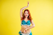 Beautiful Red-haired Woman Dancing Oriental Belly Dance In Blue Suit On Yellow Background In Studio