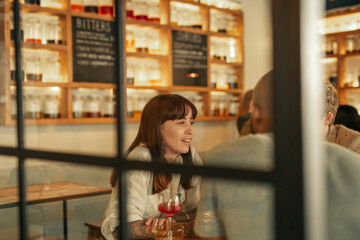 Wall Mural - Young woman talking with friends over drinks in a bar